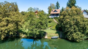 Une maison avec un toit recouvert de tuiles rouges, entourée d’une végétation luxuriante et d’un petit étang.