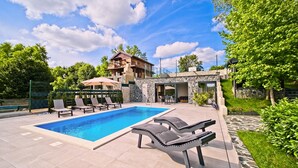 Une piscine avec des chaises longues, un bâtiment en pierre et une structure en bois dotée d’un balcon.