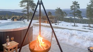 A hot tub on a wooden deck with a fire feature, surrounded by snowy landscape and houses. - Awesome home in Hønefoss with WiFi (Hønefoss)