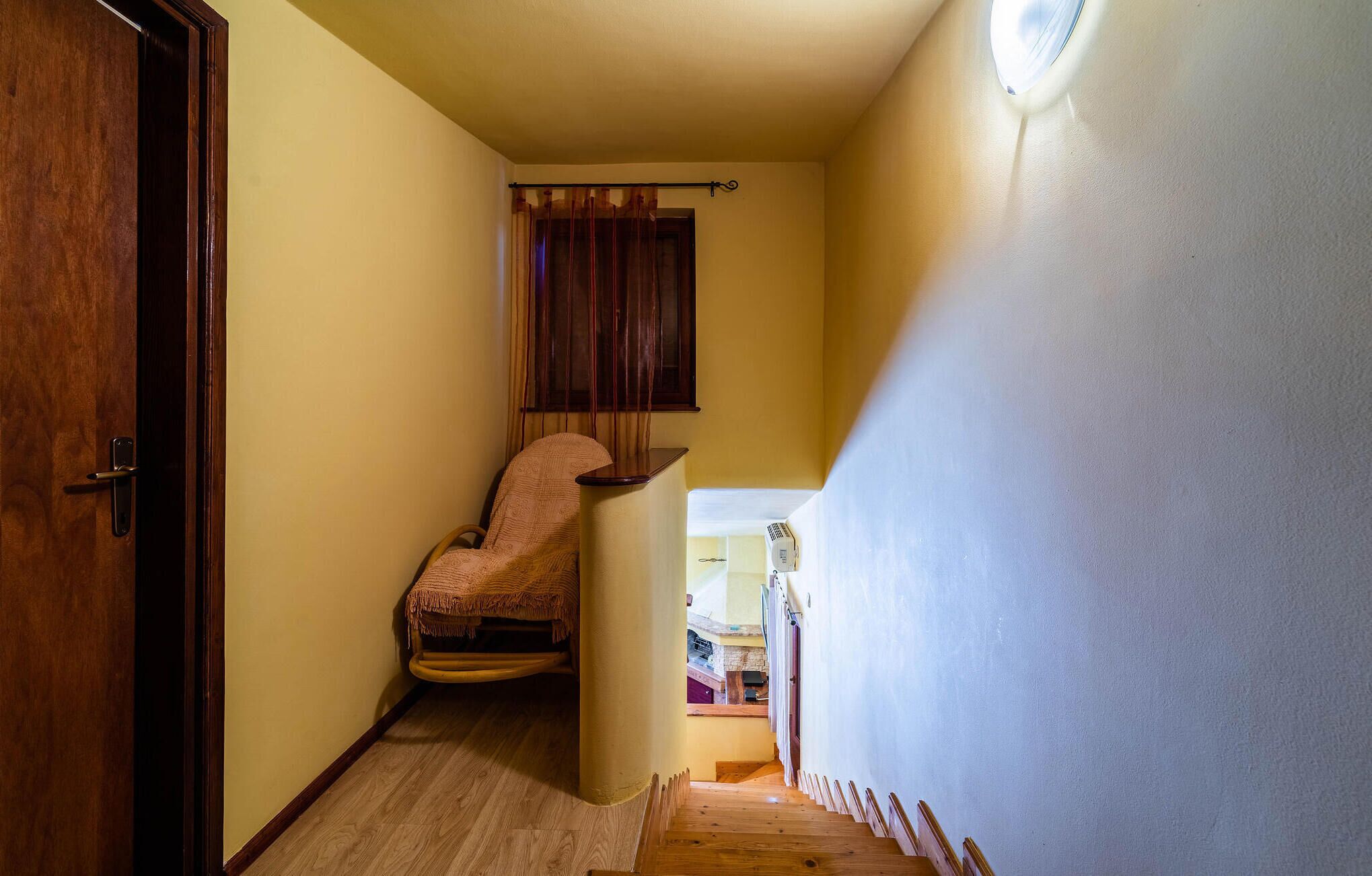 A narrow hallway with a wooden door on the left, a chair with a blanket, and a staircase leading to another room.