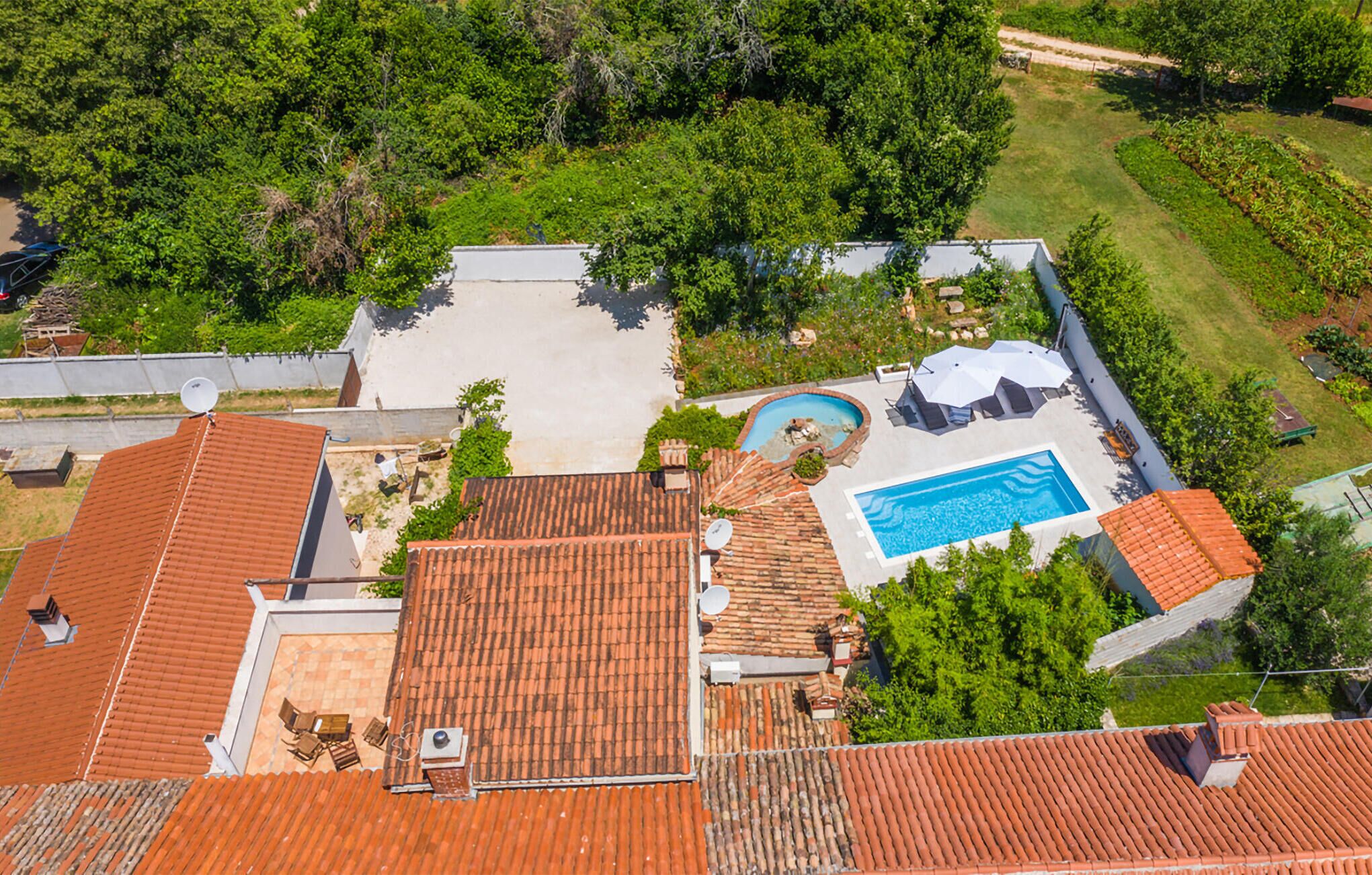 Vue aérienne d’une propriété résidentielle dotée d’une piscine, d’un espace de détente extérieur et d’un jardin.