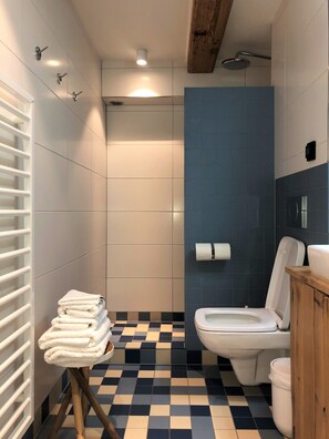 A bathroom with a checkered floor, a white toilet, a shower, and a stack of white towels on a stool. - Stay in our centrally located 18th century house. Contactless stay possible. (Amsterdam)