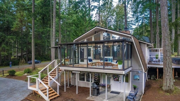 Et moderne hus i to etager med en glasindrammet veranda, en trætrap og et overdækket udendørs siddeområde.