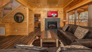 Interior de una cabaña de troncos con chimenea, sofá de cuero y televisor montado mostrando opciones de canales.