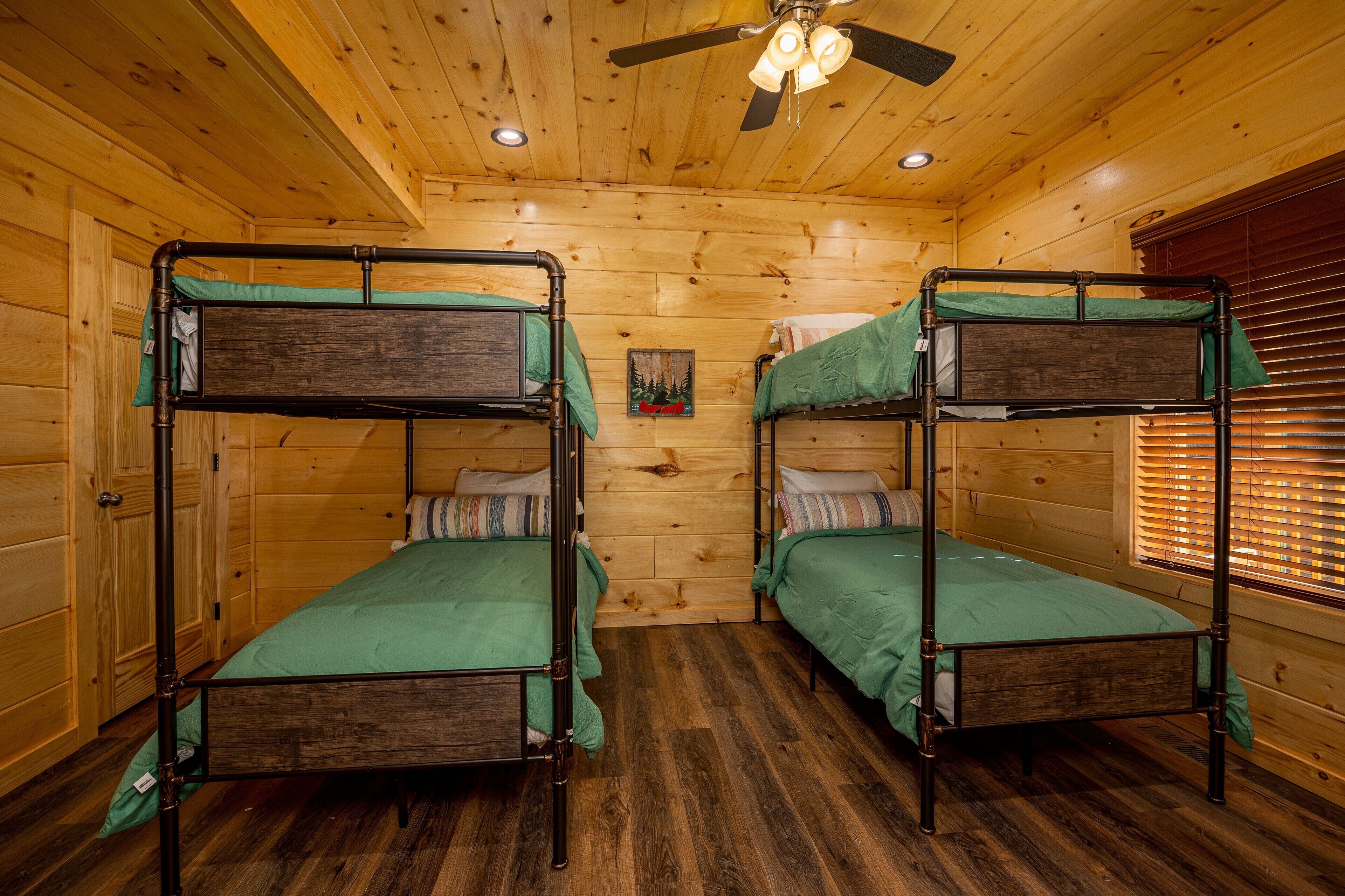 A cabin with two bunk beds, wooden walls, a ceiling fan, and a window with blinds.