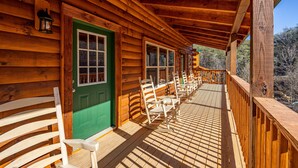 Una cabaña de madera con un porche, puerta verde y mecedoras blancas.