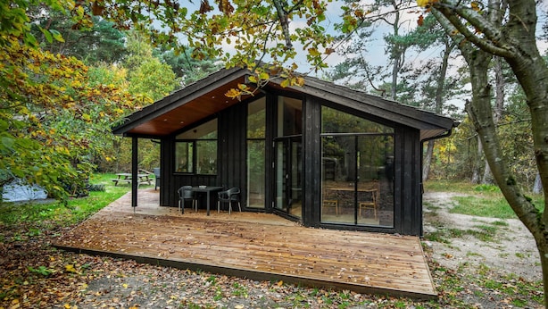 Una cabaña moderna con terraza de madera, ventanas amplias y zona de comedor.