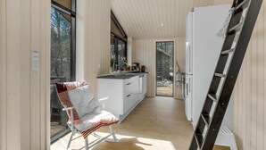 Una cocina moderna con interior de madera, una isla blanca y una escalera negra apoyada en la pared.