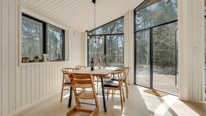 Comedor con mesa y sillas de madera, ventanas amplias y vista a los árboles.