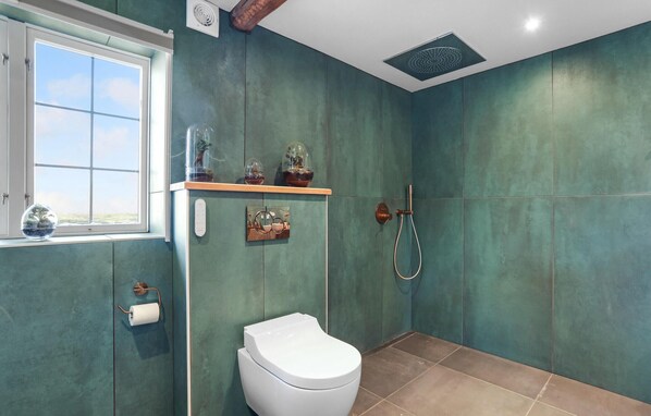 Ein Badezimmer mit türkisfarbenen Wänden, einer Toilette, einer Dusche und einem Fenster mit Aussicht.