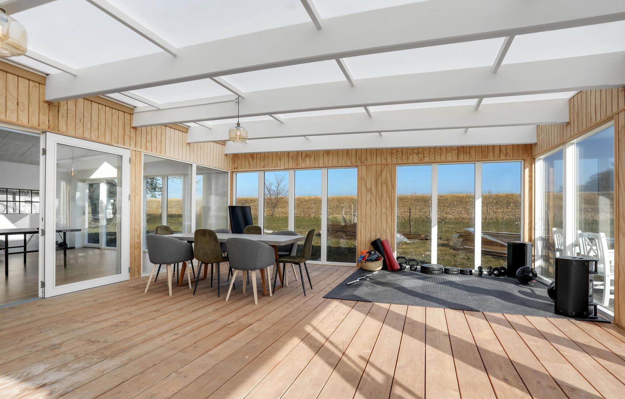 Ein modernes Zimmer mit Holzboden, einem Tisch mit Stühlen und großen Fenstern mit Blick ins Freie.