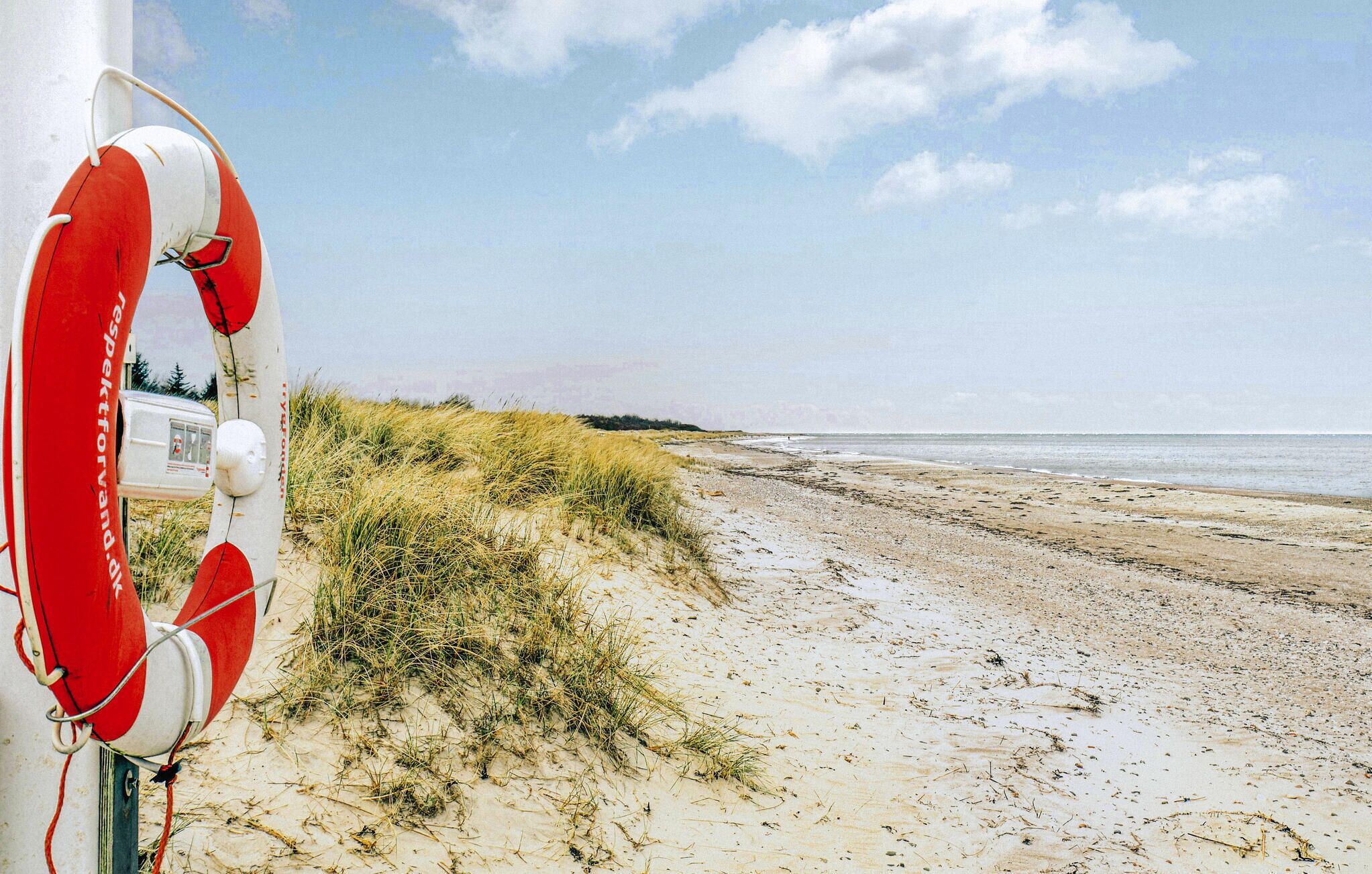 A lifebuoy attached to a pole on a sandy beach with dunes and a clear sky.