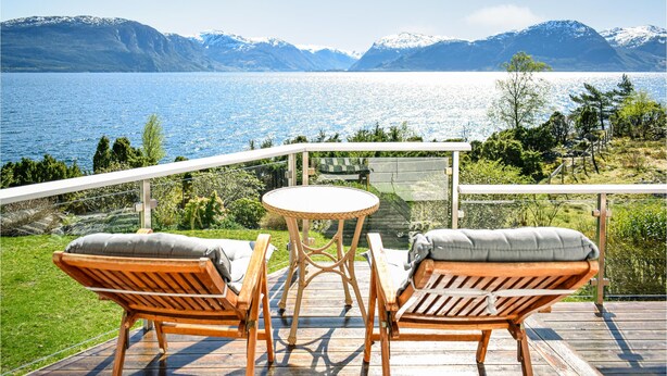 Una terraza con dos sillones de mimbre y una pequeña mesa redonda, con vista a un lago y montañas al fondo.