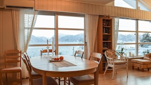 Un comedor con mesa de madera, sillas y vista a un lago con montañas al fondo.