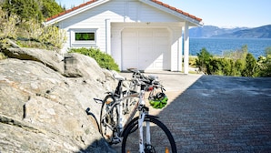 Un garaje blanco con techo rojo, una bicicleta estacionada al frente y una vista panorámica del mar y las montañas al fondo.