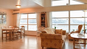 Una habitación acogedora con suelo de madera, un sofá, una mesa de comedor con sillas, una estantería y ventanas amplias que ofrecen vistas a un paisaje nevado.