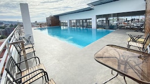 Una piscina en la azotea con agua azul cristalina, rodeada de sillones de descanso y una mesa de vidrio.