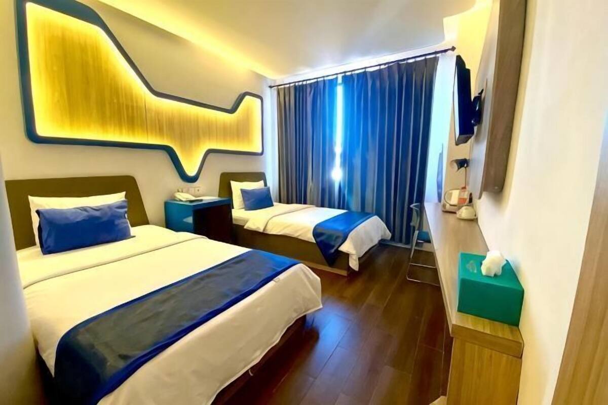 Een hotelkamer met twee bedden, een groot abstract kunstwerk aan de muur, een spiegel en een gordijn.