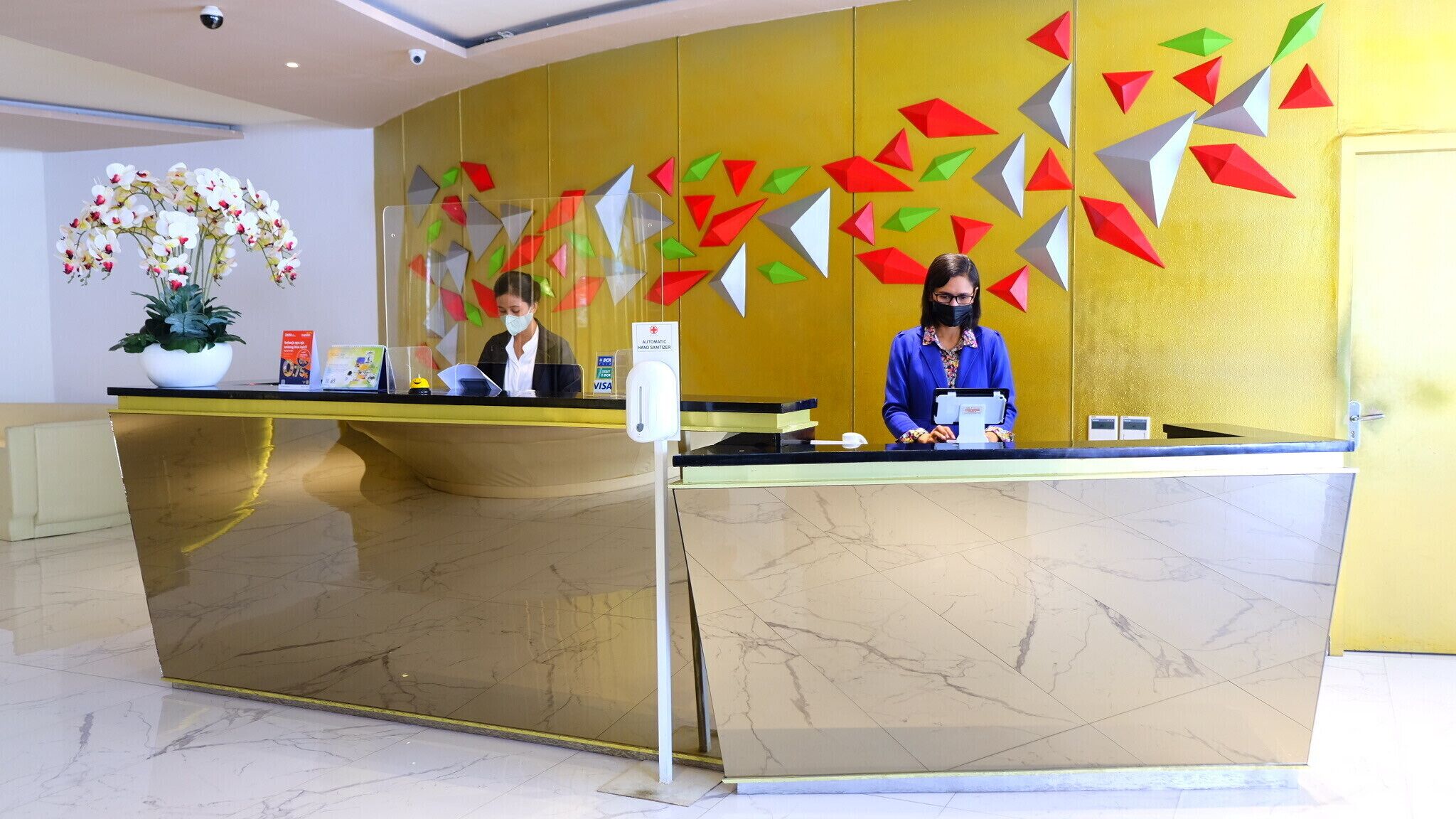 Un mostrador de recepción con suelo de mármol, una planta en maceta y una pared con decoraciones geométricas de colores.