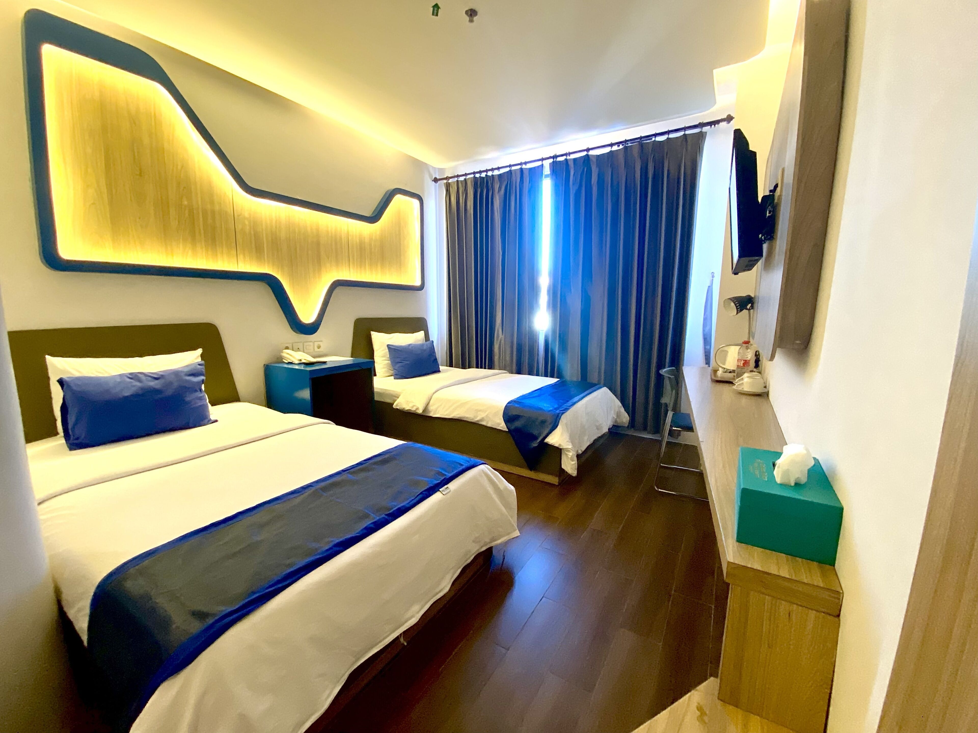 Hotellihuone, jossa on kaksi sänkyä, moderni seinäkoriste, suuri peili ja puulattia.