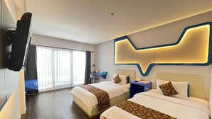 Habitación de hotel con dos camas, un escritorio, una silla, un televisor montado en la pared y un ventanal con cortinas.