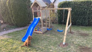 A wooden play structure with a slide and swings in a backyard. - Vacation home Weserbergland, for up to 8 persons (Höxter)