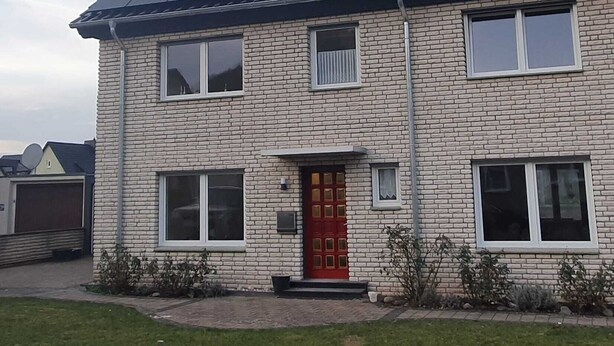 A two-story house with a red door, a satellite dish, and a solar panel roof. - Vacation home Weserbergland, for up to 8 persons (Höxter)