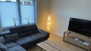 A modern living room with a sectional sofa, a wooden coffee table, a TV on a wooden stand, and a large vase. - Vacation home Weserbergland, for up to 8 persons (Höxter)
