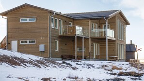 A multi-story wooden house with balconies, a sloped roof, and a small outdoor seating area.