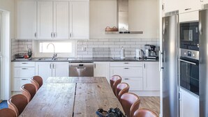 A modern kitchen with white cabinets, a stainless steel refrigerator, and a wooden dining table with leather chairs.