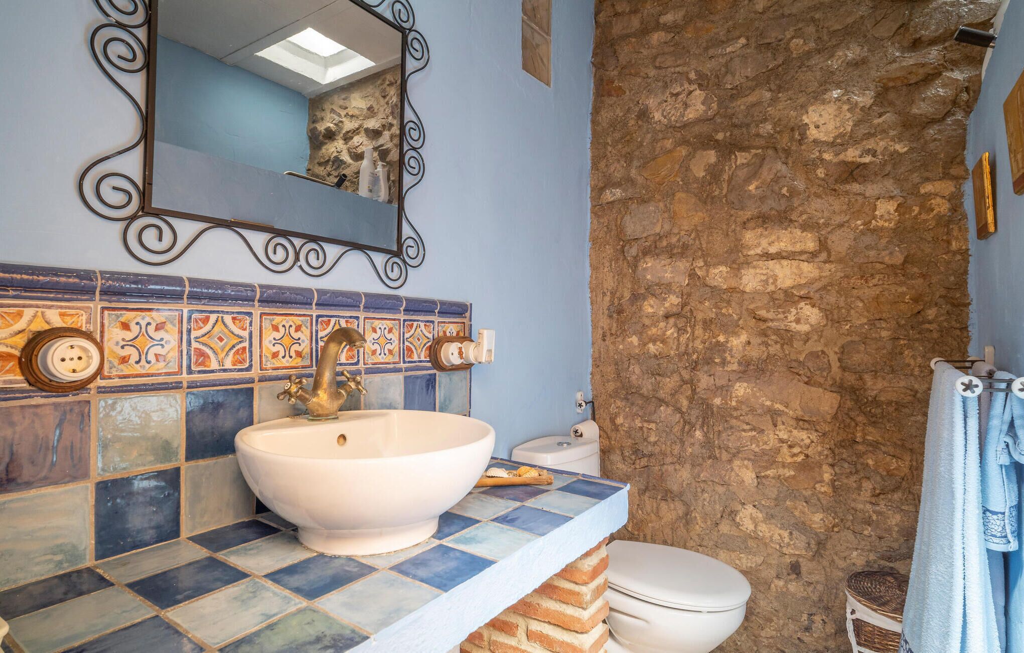 A bathroom with a white sink, a mirror, and a stone wall.