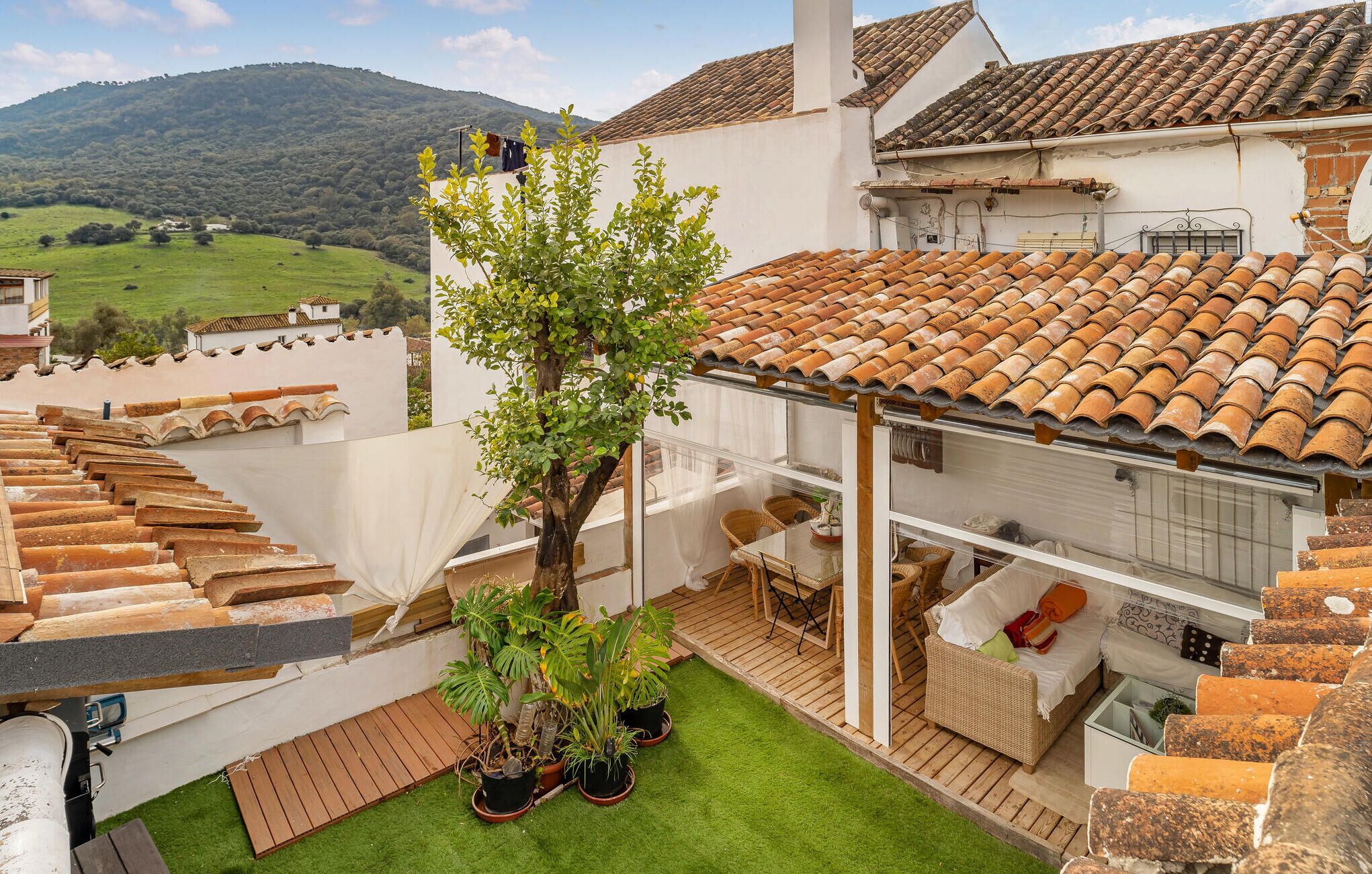 A rooftop terrace with terracotta tiles, a small tree, and a wicker sofa.