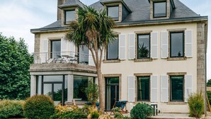 A two-story house with a balcony, large windows with shutters, and a well-maintained garden.