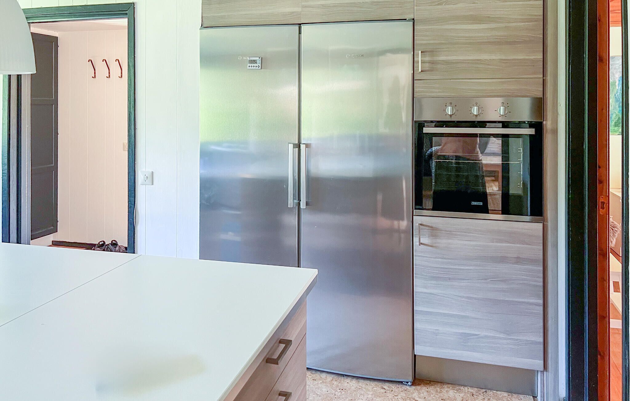 A modern kitchen with a stainless steel refrigerator and oven, a white countertop, and wooden cabinetry.