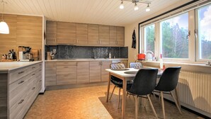 Een moderne keuken met houten kastjes, een eettafel met stoelen, en een groot raam met uitzicht op het landschap.