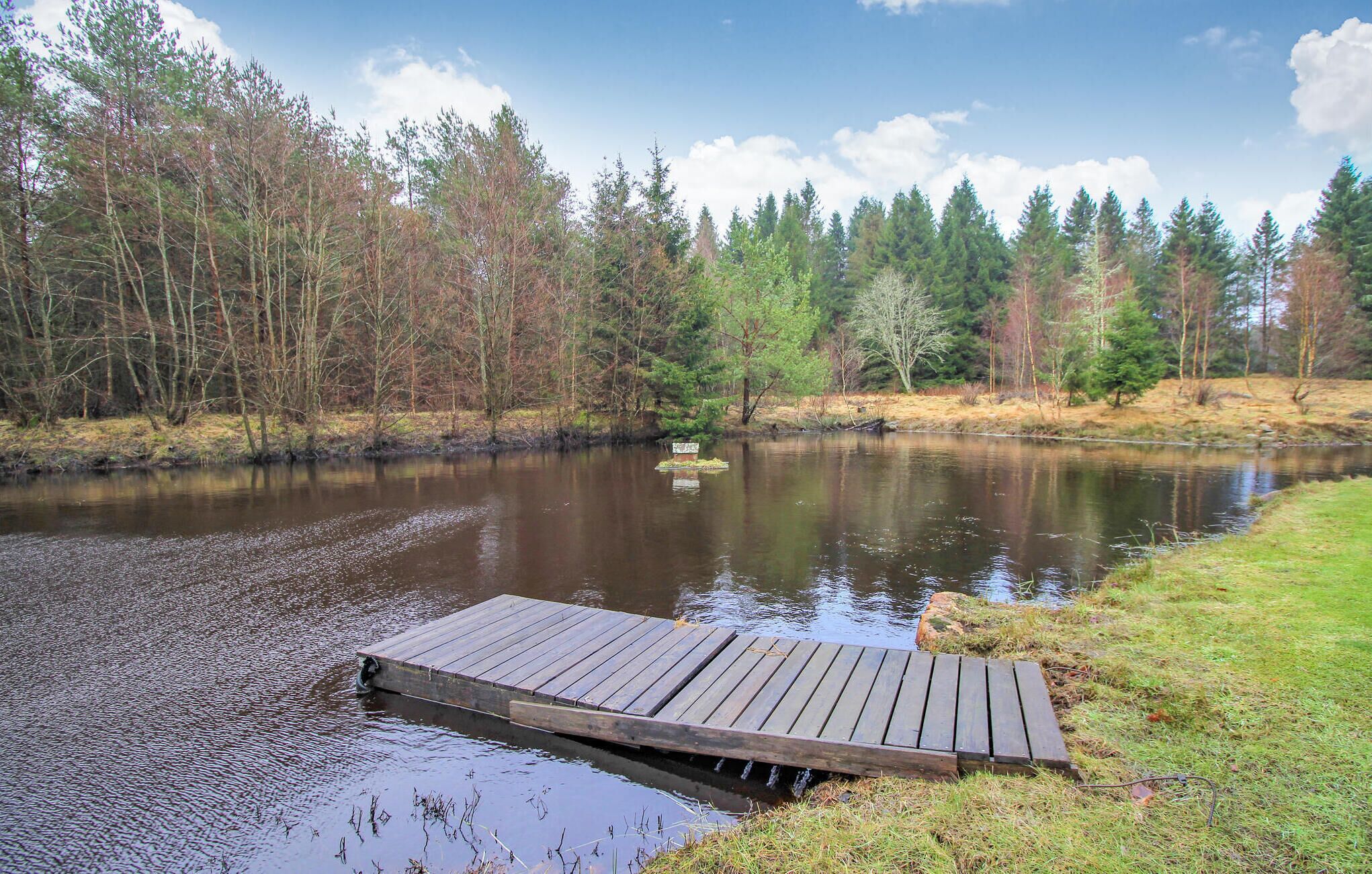 A wooden dock extending into a calm river surrounded by a forest.