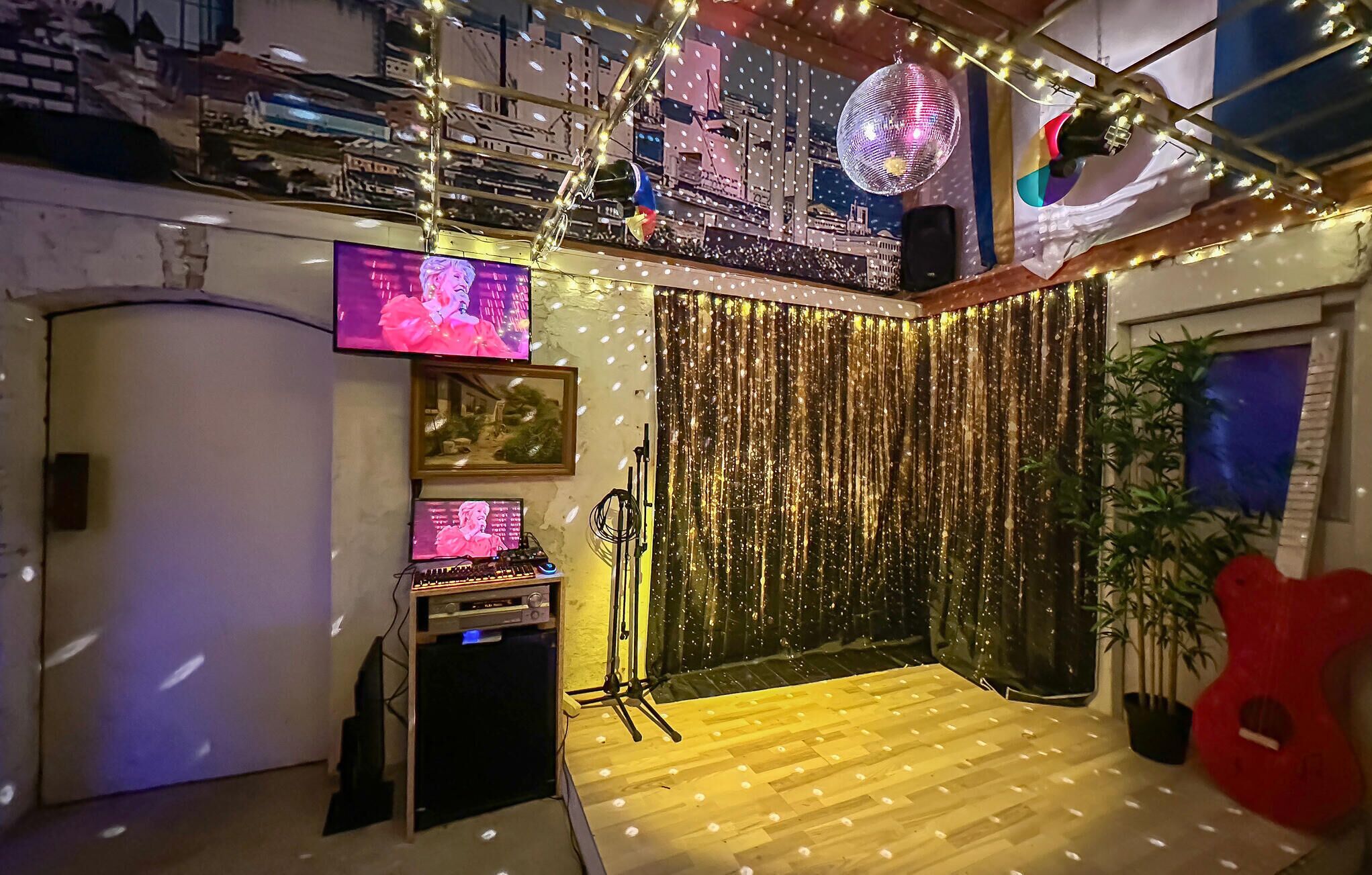A room with a wooden floor, a DJ setup, a television, and a disco ball.