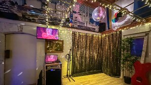 Een kamer met een houten vloer, een DJ-installatie, een televisie en een discobal.