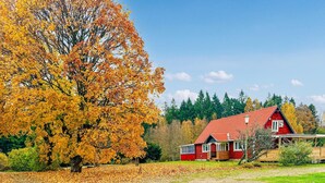 Een rode woning met een schuin dak, omgeven door herfstkleurige bladeren en een heldere lucht.