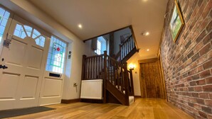 A spacious hallway with wooden flooring, a staircase, and a brick wall.
