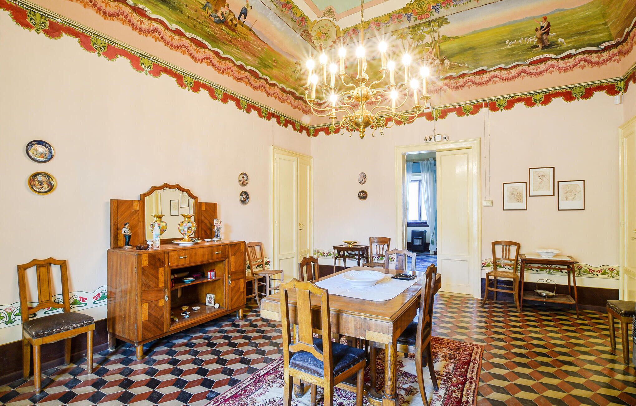 Une salle à manger avec un sol à carreaux, des meubles en bois, un lustre et une fresque au plafond.