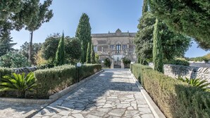 A stone pathway leading to a historic building with a grand entrance, surrounded by neatly trimmed hedges and cypress trees. - Awesome home in Modica (Modica)