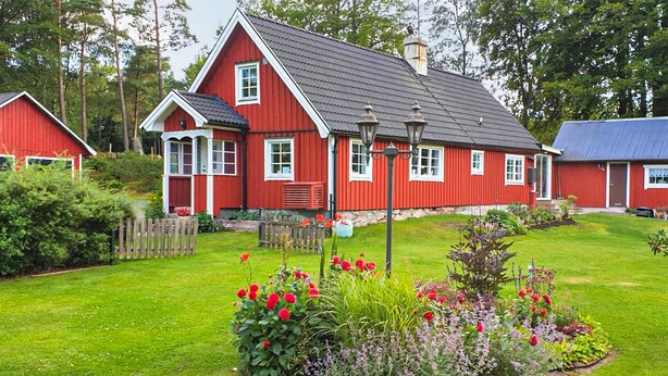 A red house with a sloped roof, surrounded by a well-maintained garden with various plants and flowers. - Pet friendly home in Perstorp with WiFi (Perstorp)