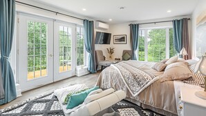 Een ruime slaapkamer met een groot bed, een bureau en een stoel. Er zijn twee ramen met gordijnen en een airconditioningunit aan de muur.