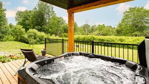Een hottub op een houten terras met uitzicht op een verzorgd gazon en bomen.