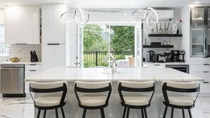 Een moderne keuken met witte kasten, een groot eiland met barstoelen en uitzicht op groen.