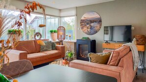 Ein modernes Wohnzimmer mit Sofa, Couchtisch und Kamin. Ein Fernseher und ein Bücherregal sind ebenfalls vorhanden.