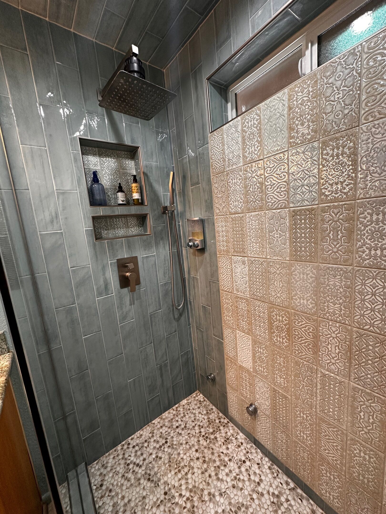 Ein Badezimmer mit Dusche, Waschtisch mit Spiegel und Wand mit gemusterten Fliesen.