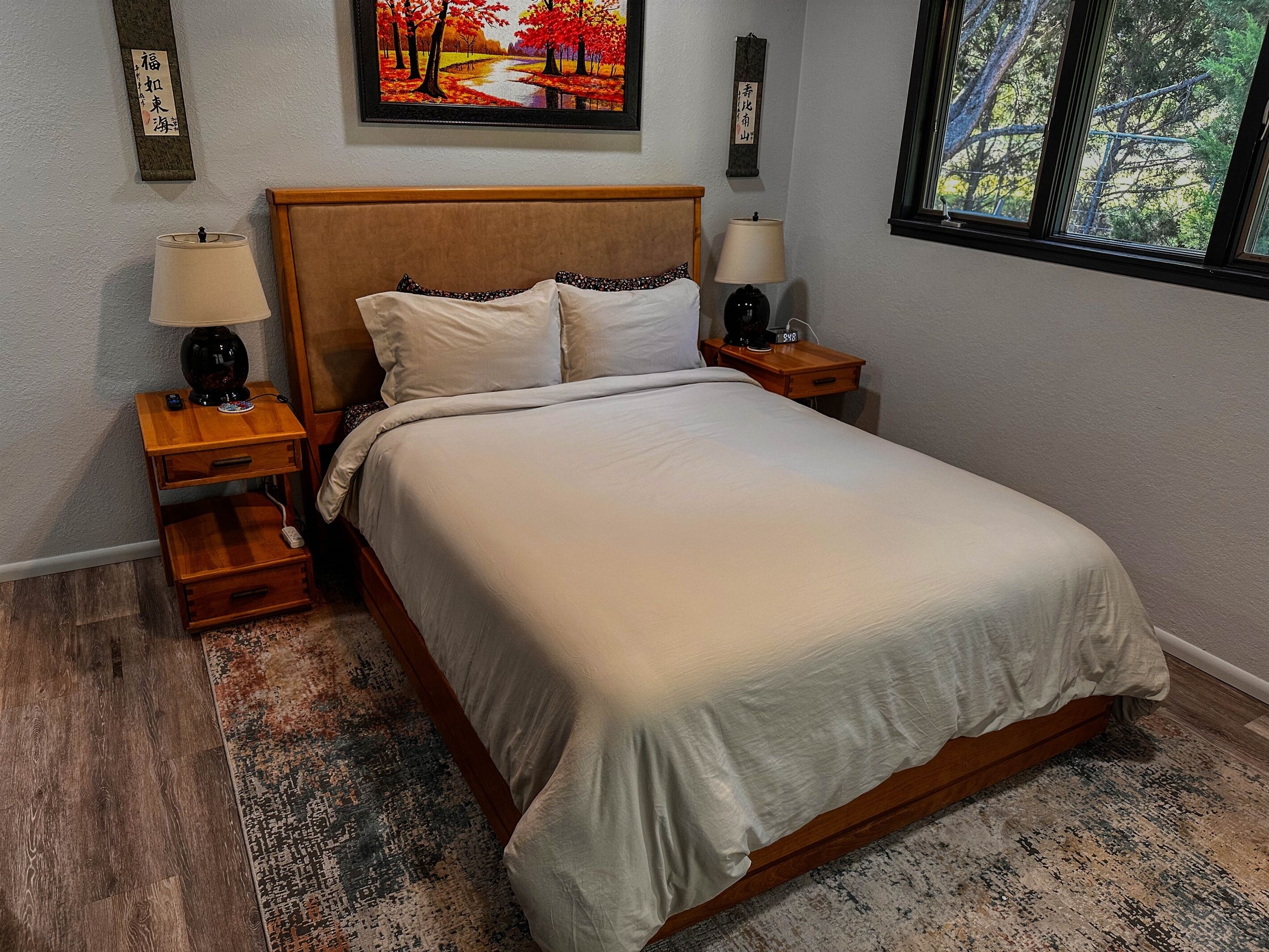 A bedroom with a wooden bed, two bedside tables with lamps, a rug, and a painting on the wall.