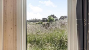 A room with a large window overlooking a grassy field with trees and a building in the distance. - 3 bedroom beautiful home in Blåvand (Blåvand)